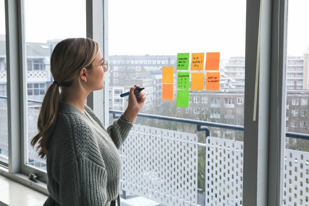 Mujer joven escribiendo en notas adhesivas dispuestas en una ventana